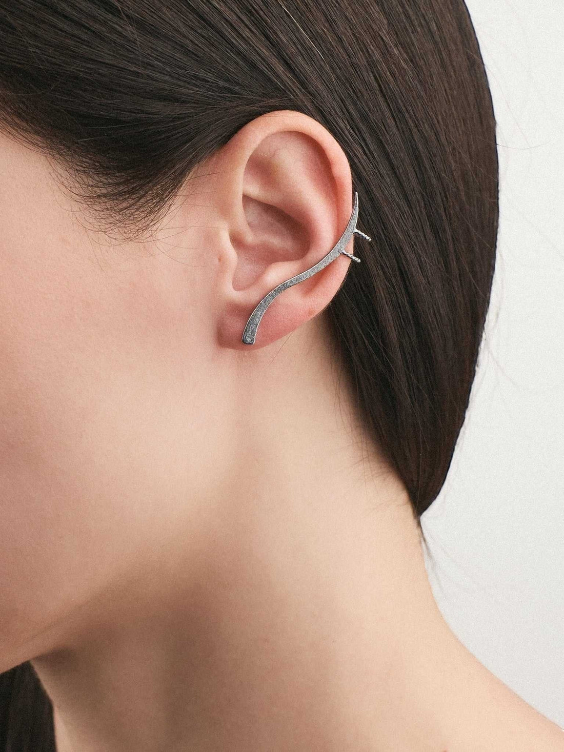 Jouly K abstract silver ear cuff with a flowing, sculptural design worn on a model's ear for a modern look.
