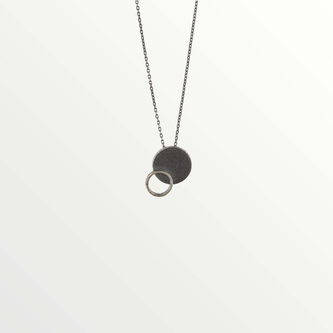 Jouly K silver necklace with oxidized finish, featuring a large disc pendant and a smaller textured ring.